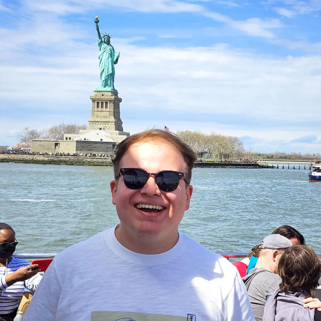 Hombre sonriendo frente a la estatua de la libertad